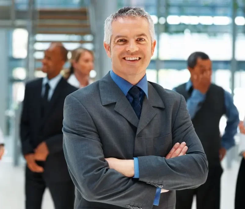 A confident senior executive standing with arms crossed in a bright office